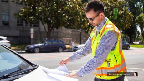 Person in safety vest reading documents on the hood of their car